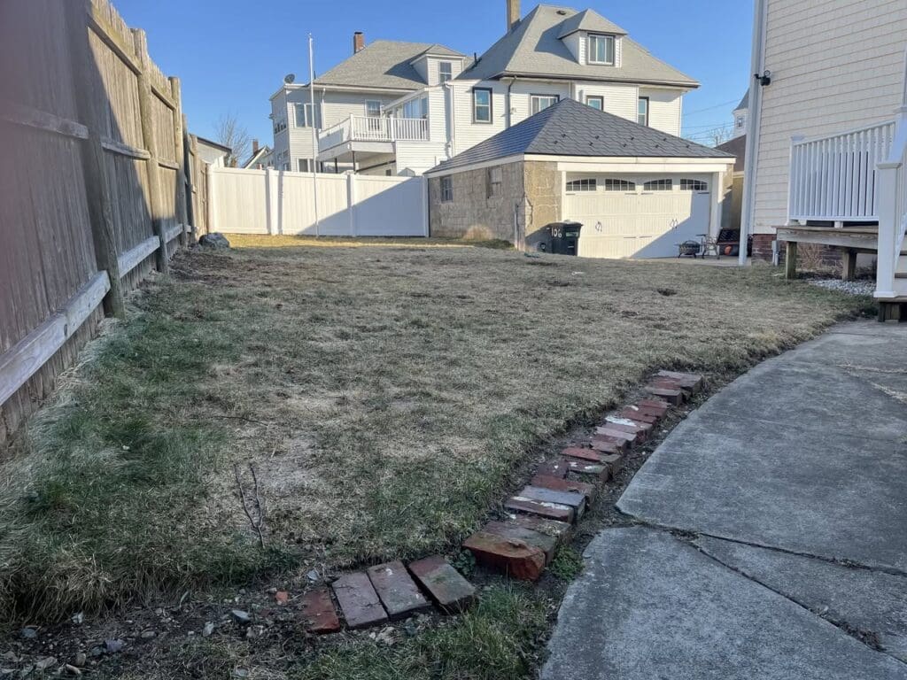 Backyard with patchy grass and uneven lawn before landscaping upgrade on the North Shore of Massachusetts