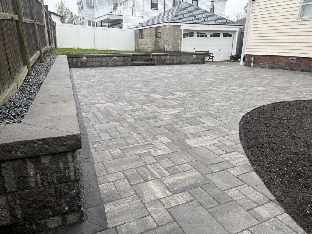 Fully landscaped backyard with new paver patio, retaining wall, and clean edging after professional landscaping in North Shore MA
