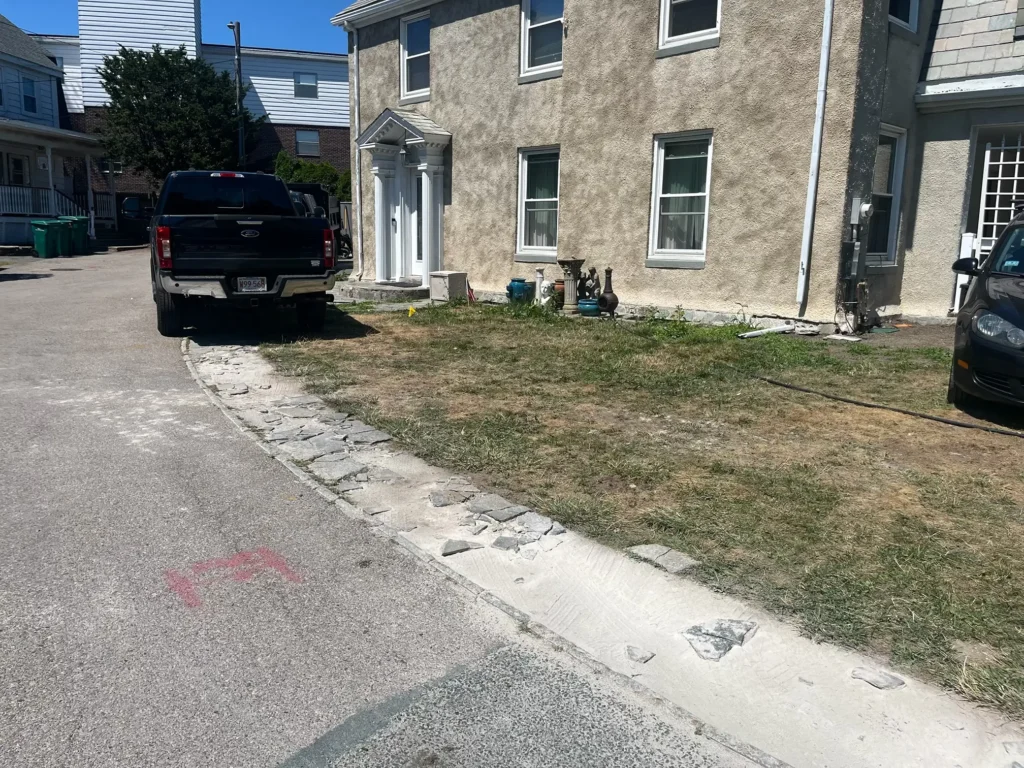 A patchy, dry lawn and broken concrete curb in Lynn, MA, before a full landscape renovation by Leahy Landscaping.